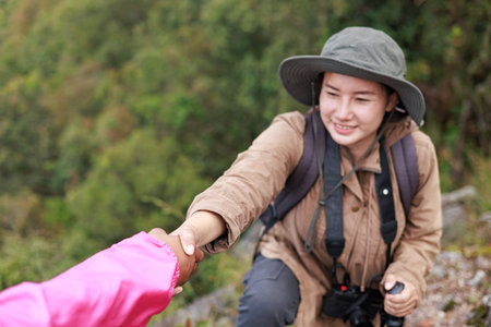 Two hikers on rocky mountain peak helping each other climb, symbol of teamwork, leadership, support,...