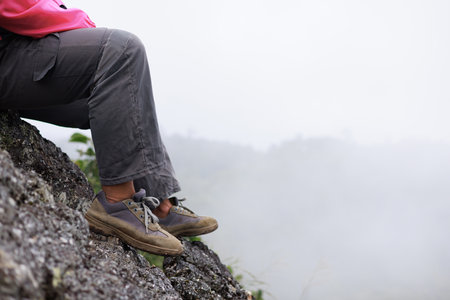 Close up of hiker resting on rocky cliff in hiking shoes, symbol of adventure, outdoor lifestyle, challenge, exploration, determination, nature journey and freedom in mountain travel.の写真素材