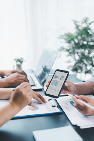 Business data analysis concept with colleagues reviewing financial report on smart phone, pointing at chart with growth graph, teamwork discussing statistics, planning strategy and corporate success.の写真素材
