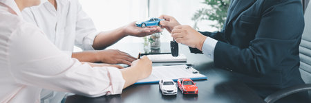 Panorama view of car dealer handing key and vehicle model to customer during contract signing,...