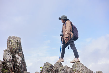 Hiker standing on rocky cliff with trekking pole, symbol of adventure, confidence, challenge, exploration, outdoor lifestyle, success and travel inspiration in mountain nature.の写真素材
