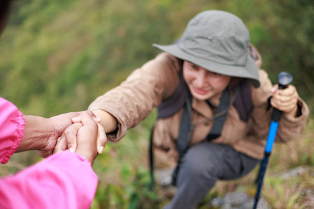 Two hikers on rocky mountain helping each other climb, symbol of teamwork, leadership, support, adventure, success, trust, exploration and outdoor lifestyle motivation in nature.の写真素材