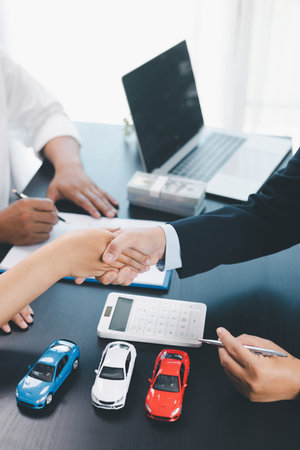Business handshake after signing car loan contract, symbol of trust and successful auto finance agreement with money, calculator and vehicle model on desk, concept of deal and partnership. car loan.の写真素材
