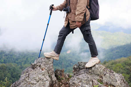 Close up of hiker standing on rocky cliff with trekking pole, symbol of adventure, confidence, challenge, exploration, outdoor lifestyle, success and travel inspiration in mountain nature.の写真素材