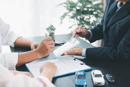 Businessman explaining car loan agreement with calculator, customer discussing auto finance deal at office desk with toy car and document, concept of vehicle loan, insurance or car leasing. car loan.の写真素材