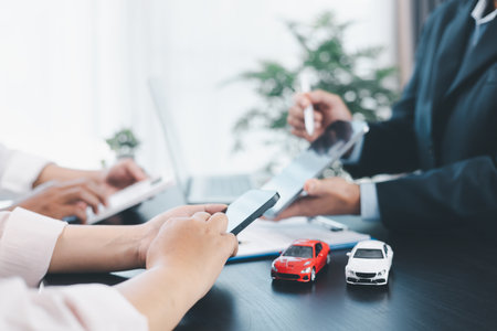 Car loan officer explaining contract details to customer with cash, calculator, key and toy car on table, concept of auto finance, leasing, insurance, payment plan and business agreement. car loan.の写真素材