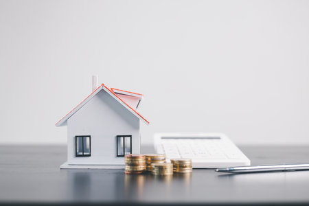 House models with stacked coins in front, symbolizing mortgage loan, real estate investment, property finance, housing economy, wealth, savings, construction planning concept on minimal background.の写真素材