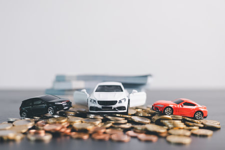 Three car models in red, black and white placed on stacks of money with scattered coins, representing auto loan, car finance, investment, insurance, leasing, savings concept. car finance, investmentの写真素材