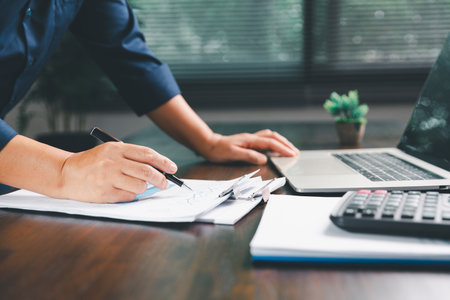 Office businesswoman hand to operate calculator analyzing financial data, counting costs on desk. accounting, financial analysis for business budget planning, calculation support, finance management.の写真素材