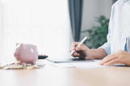 Concept of saving money and financial security. Pink piggy bank surrounded by coins on office desk with businesswoman in background, symbolizing investment, wealth growth and budget management.の写真素材
