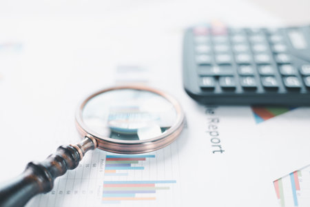 Magnifying glass with calculator and pen on financial reports with charts, graphs at office desk. Concept of business analysis, accounting audit, financial accuracy, transparency, corporate strategy.の写真素材