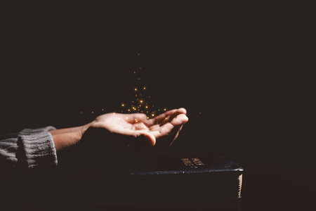 Open hand with glowing light above the Holy Bible, symbolizing prayer, blessing, faith, Christianity, divine hope and spiritual strength from God Word and holy guidance.の写真素材