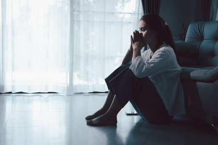 Tired depressed desperate tired girl sadly sitting on couch at home. Young woman is sitting on floor living room, feeling sad and depressed. Psychological problem. Depression and loneliness concept.の写真素材