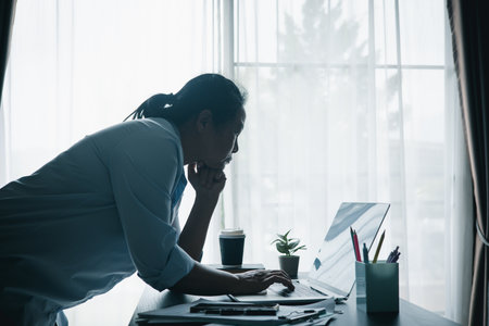 Stressed businesswoman working late at home office, feeling exhausted while reviewing financial...