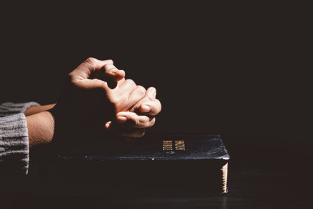 Hands clasped in prayer over the Holy Bible, symbolizing faith, devotion, Christianity, hope and...
