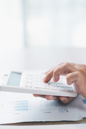 Close up of businesswoman using calculator for financial analysis and accounting on office desk with charts and reports. Concept of business planning, budget calculation and investment strategy.の写真素材