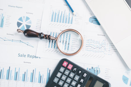 Magnifying glass with calculator and pen on financial reports with charts, graphs at office desk....