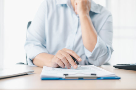 Concept of tax filing and financial documentation. Close up of businesswoman hand holding pen and pointing on tax form, symbolizing accounting, legal paperwork, budget planning and financial accuracy.の写真素材