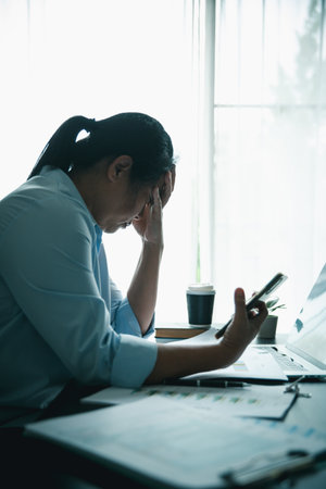 Stressed businesswoman working late at home office, feeling exhausted while reviewing financial...