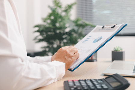 Businessperson using calculator and laptop with financial report on office desk, concept of accounting analysis, budget planning, data management and corporate finance strategy.の写真素材