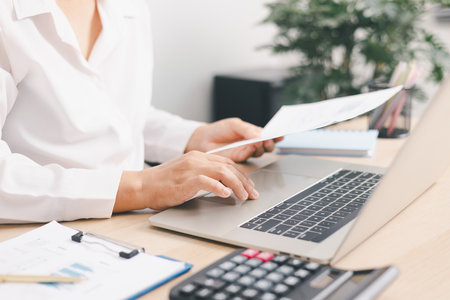 Businessperson typing on laptop with financial report and pen on office desk, concept of data...