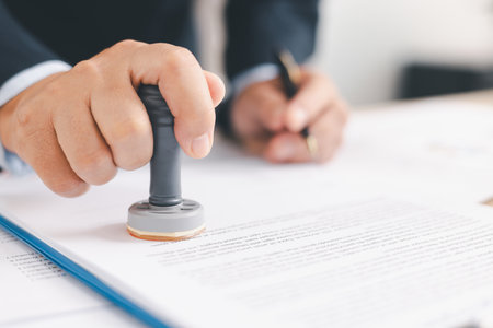 Businessman signing and stamping official document at desk, concept of legal contract approval,...