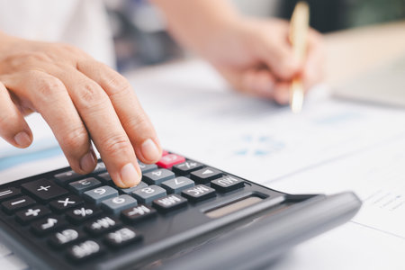 Businessperson using calculator and laptop with financial report on office desk, concept of accounting analysis, budget planning, data management and corporate finance strategy.の写真素材