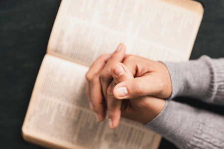 Hands in prayer above Holy Bible on wooden table, symbolizing Christian faith, worship, devotion,...