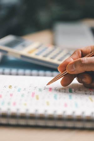 Hand writing notes in a notebook beside a calculator on office desk for budgeting and accounting....