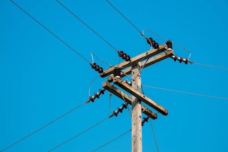 electrical post by the local road with power line cables in bright and clear blue sky.の写真素材