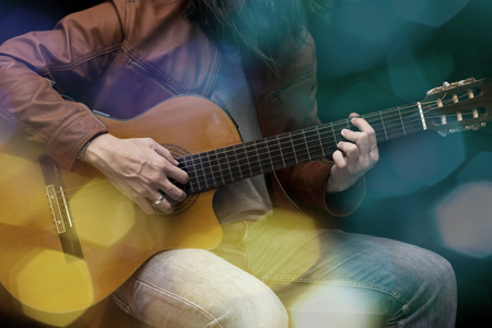 Long hair male guitarist playing with acoustic guitar in leather jacket on the stage.の写真素材
