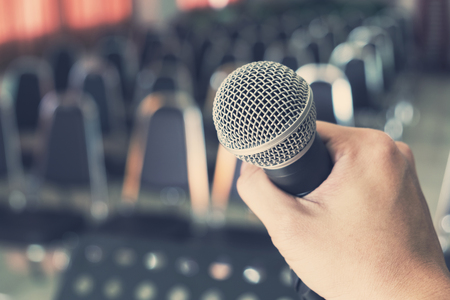 Man Holding Microphone over the Blurred Chairs in the Conference hall or Seminar Indoor Room Background.の写真素材