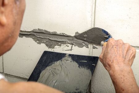 Skillful Old Man Plasterer Plastering Cement on the Old Brick Wall.