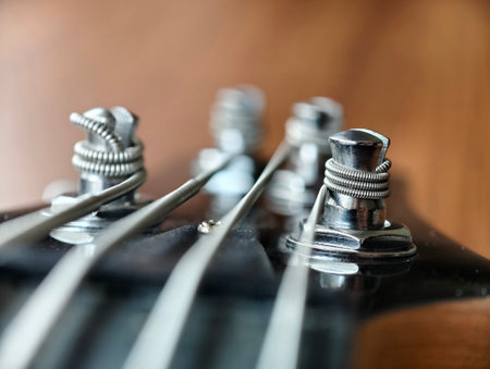 Macro close-up of bass guitar headstock showing tuning pegs, strings, and metallic details. Musical...