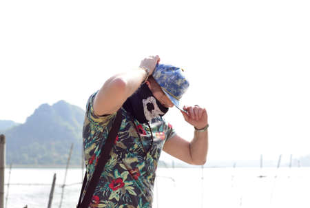 Young man guy in casual t-shirt, cap and face mask posing on nature background. Traveling lifestyle...