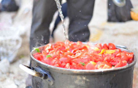 Pouring water into the saucepan with fresh red tomatoes. Selective focus.