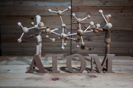 wooden puppets with atom word and atom construction on wood table in wood scene