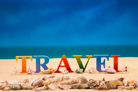 travel written in colorful letters with sea shell at the beach with copy spaceの写真素材