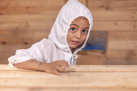 a cute long haired boy wearing a white shirt with a hood in wooden backgroundの写真素材