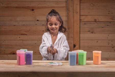 a long haired boys are enjoying using an air pump to blow powder that is placed on a wooden table.