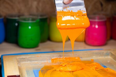 
orange color dripping from hand screen printing during printing tee shirt 
in tee shirt factory.の写真素材