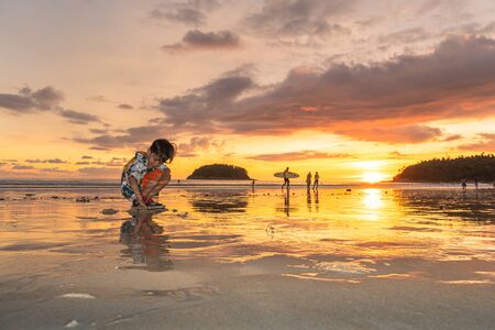 A cute boy playing sand on Kata beach,Phuket at sunset time.