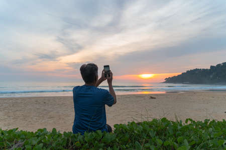A man sitting on the beach and selfie during sunset at Karon beachの写真素材