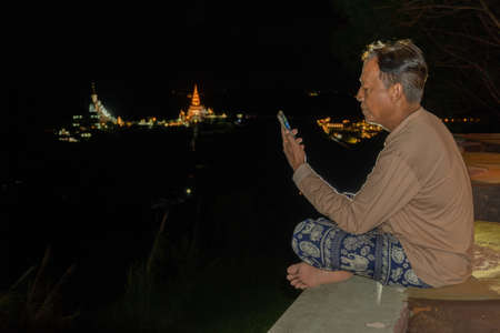 A man sitting with a mobile phone in the night.の写真素材