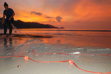 People come out to trawl their nets on Patong beach during sunset timeの写真素材