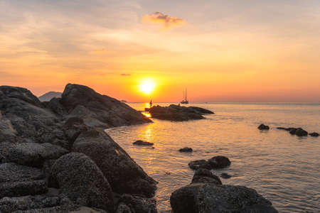 during sunset Villagers stand fishing on the rocks at Kalim Beach, next to Patong Beach. Phuket. 
During the time of the coronavirus outbreak, people have to rely on natural food to survive.の写真素材