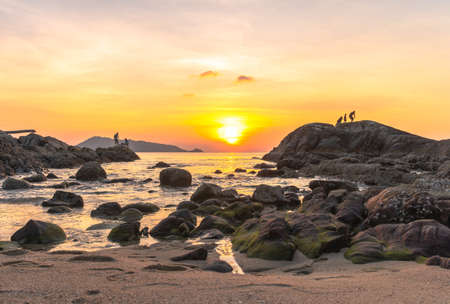 During the sunset, some people come to rest. Some come fishing on the rocks at Kalim Beach, next to Patong Beach, Phuket.の写真素材