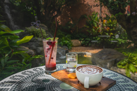 A set of hot coffee drinks placed on a ceramic table. The backdrop of a waterfall, lush greenery, and steam floated out to make it look fresh.の写真素材