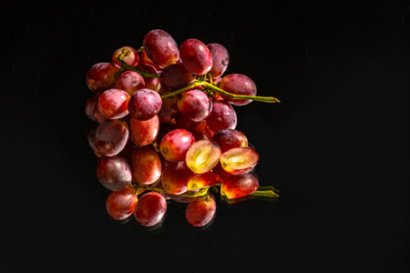 A bunch of grapes placed on the mirror with a black background