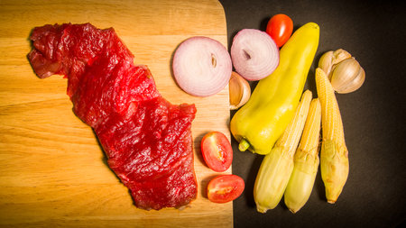 Fresh meats, vegetables and spices are laid out on a food prep table covered with a black tablecloth.の写真素材